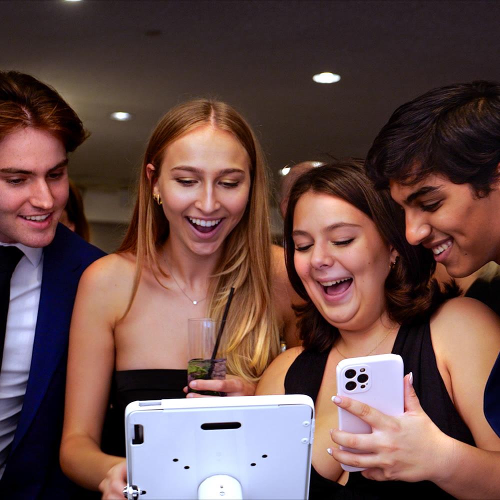 Four formally dressed guests smiling while looking at a phone beside a Viewso tablet