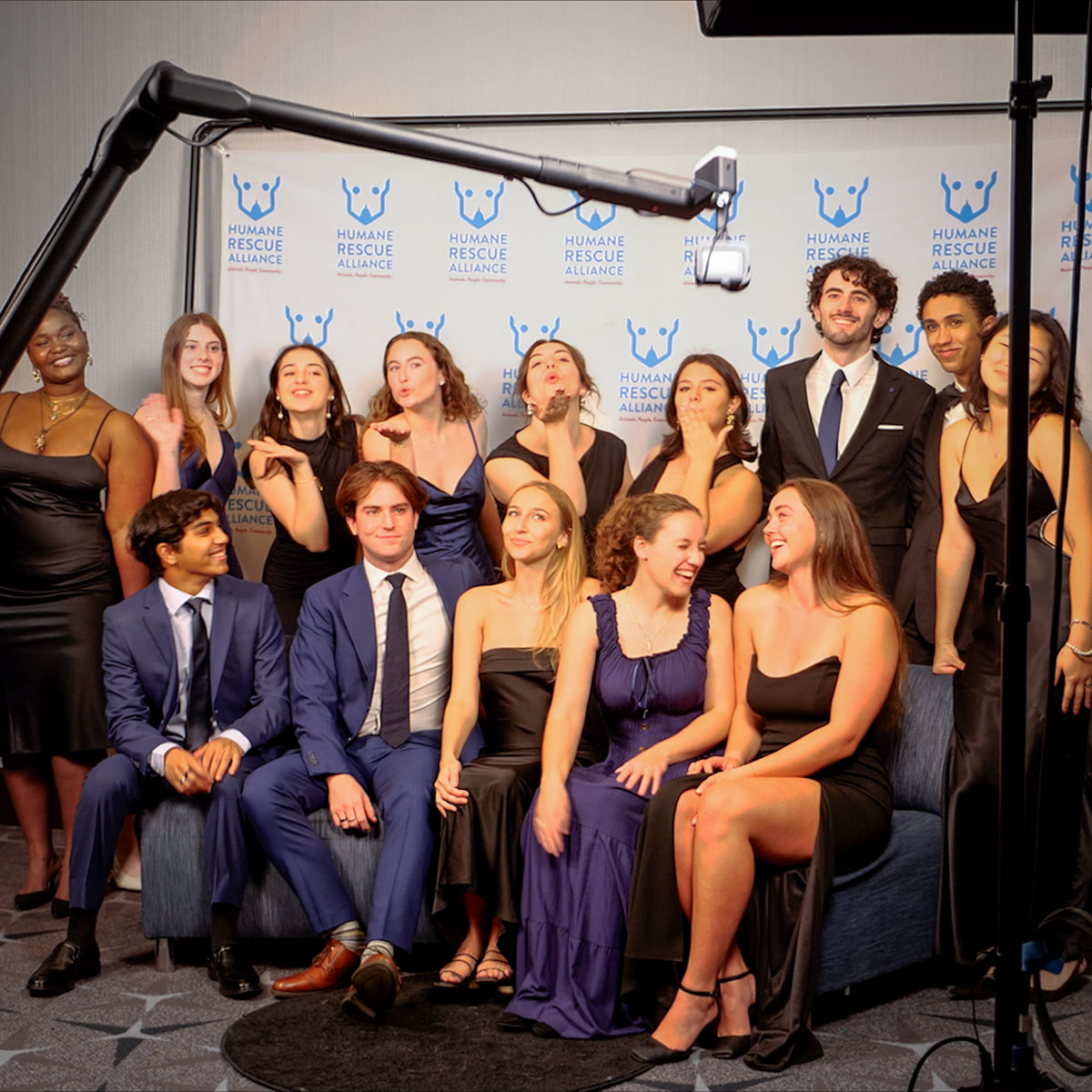 A group of formally dressed guests posing beneath the Viewso robotic camera in front of a Humane Rescue Alliance backdrop