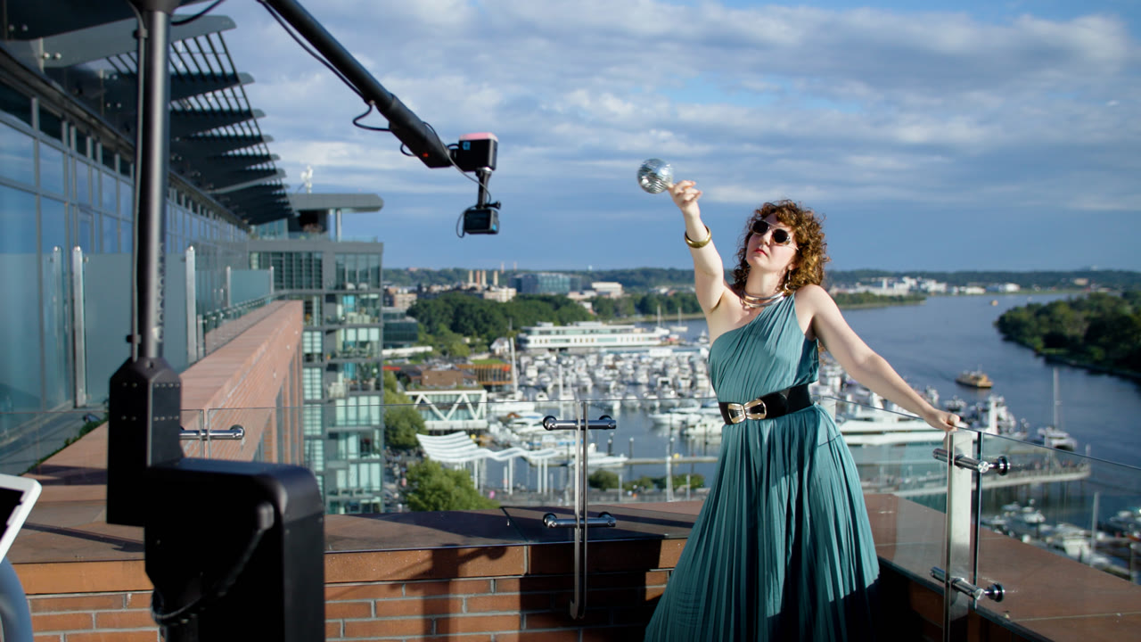 A guest in a teal dress posing beside the Viewso robotic Glambot camera on a rooftop terrace overlooking the waterfront